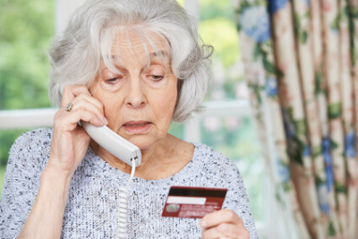 mulher idosa falando pelo telefone e com cartão de crédito na mão
